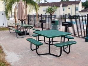 Ein Picknicktisch steht auf einer Ziegelterrasse, im Hintergrund ist ein schwarzer Metallzaun zu sehen.