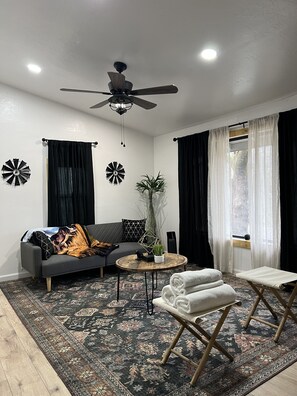 A modern living room with a grey sofa, a round coffee table, a ceiling fan, and a large window with sheer curtains. - Modern Cabin w Mountain View 3.5 MILES to Sequoia NAT’L Prk! (Three Rivers)