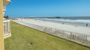 A beach with a pier, a grassy area, and a white fence. - Ocean Front Oasis with pool access~ Salty Sanctuary (Folly Beach)