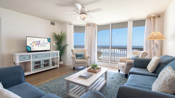 A living room with a television, sofas, a coffee table, and a balcony with a view. - Ocean Front Oasis with pool access~ Salty Sanctuary (Folly Beach)
