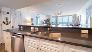 A modern kitchen with a stainless steel sink, white cabinetry, and a built-in dishwasher. - Ocean Front Oasis with pool access~ Salty Sanctuary (Folly Beach)