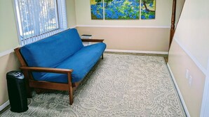 A room with a blue sofa, a patterned rug, a painting of a landscape, and a window with blinds. - Riverside cottage, minutes from historic Harpers Ferry!  Private river access! (Harpers Ferry)