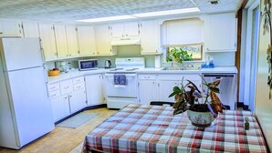 A compact kitchen with white cabinets, a microwave, stove, and a dining table with a plaid tablecloth. - Riverside cottage, minutes from historic Harpers Ferry!  Private river access! (Harpers Ferry)