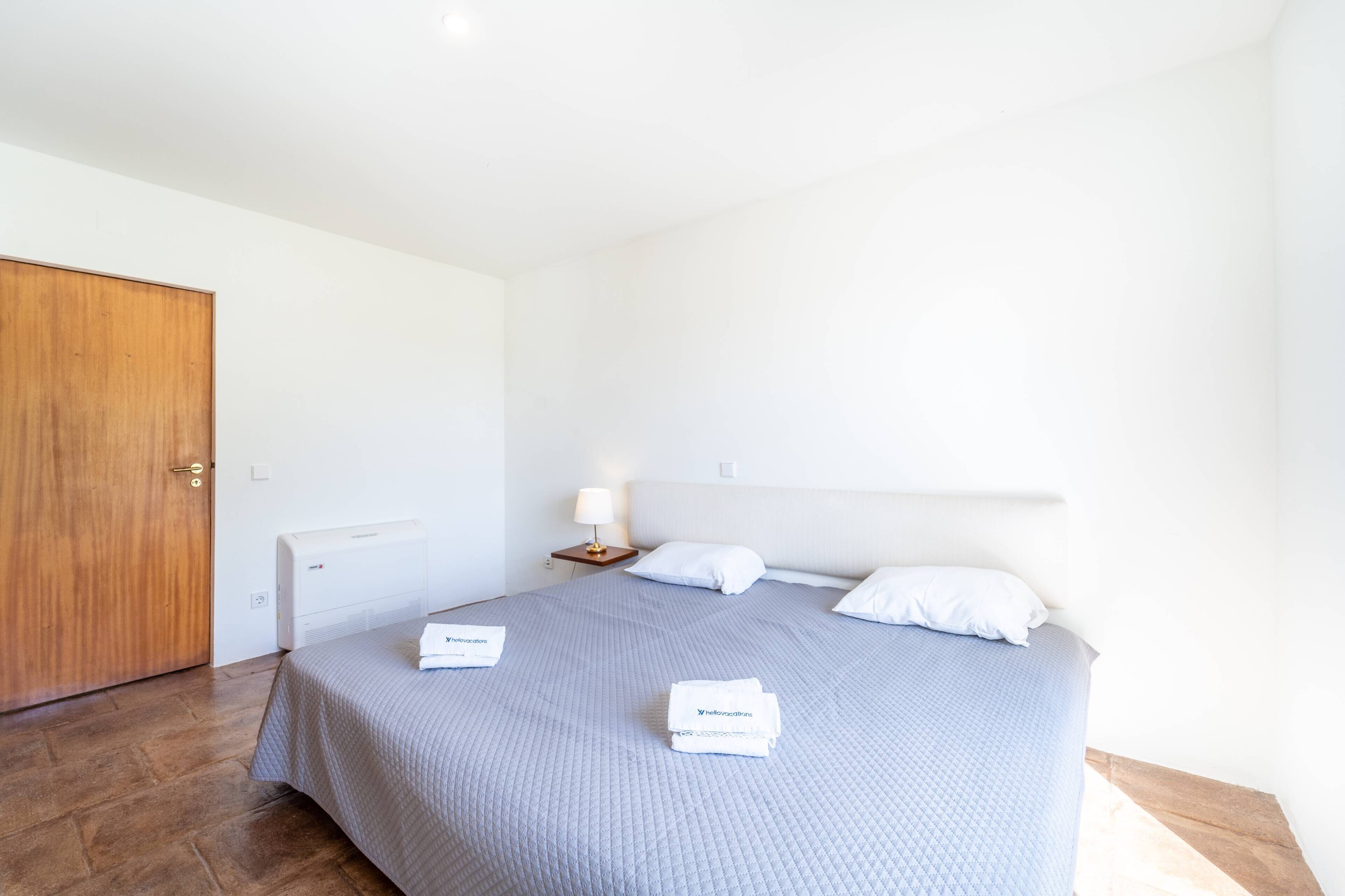 A hotel room with a bed, a wooden door, a bedside table with a lamp, and a white wall.