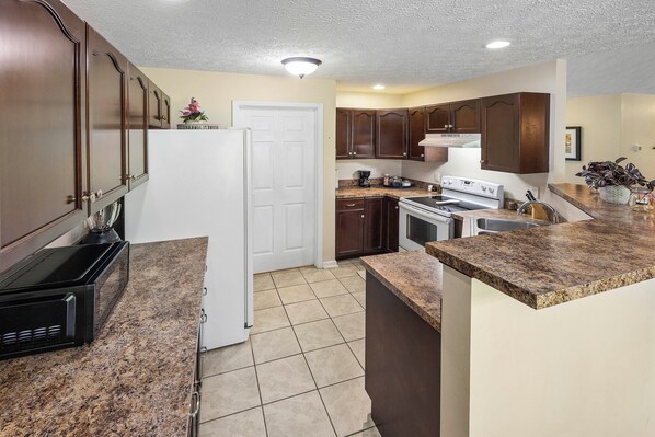 A kitchen with granite countertops, a refrigerator, a stove, and wooden cabinets. - peaceful farmhouse with hot tub (Dandridge)