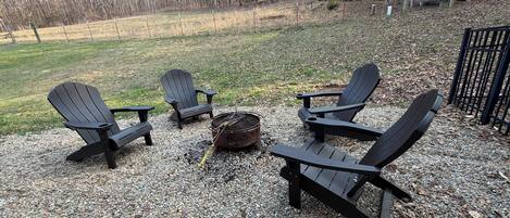 Eine Schotterterrasse mit vier Adirondack-Stühlen und einer Feuerstelle.