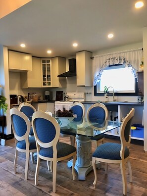 A modern kitchen with white cabinets, a glass-top dining table, and blue upholstered chairs.