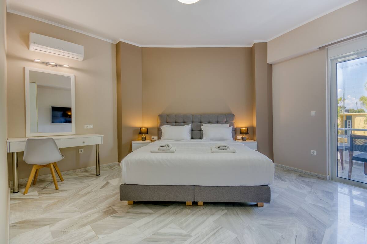 A bedroom with a bed, bedside tables, a desk, a chair, and a large mirror.