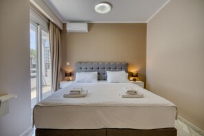 Quarto de hotel com uma cama grande, duas luminárias de cabeceira, uma janela com cortinas e um aparelho de ar condicionado na parede.