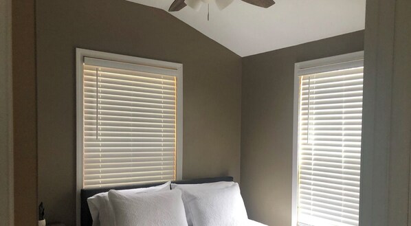 A bedroom with two windows, a bed with white linens, and a ceiling fan.