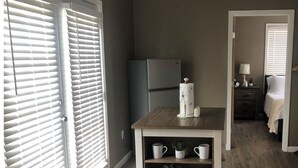 Un espace de vie compact comprenant un coin cuisine, une petite table agrémentée d’objets décoratifs et un lit en arrière-plan.
