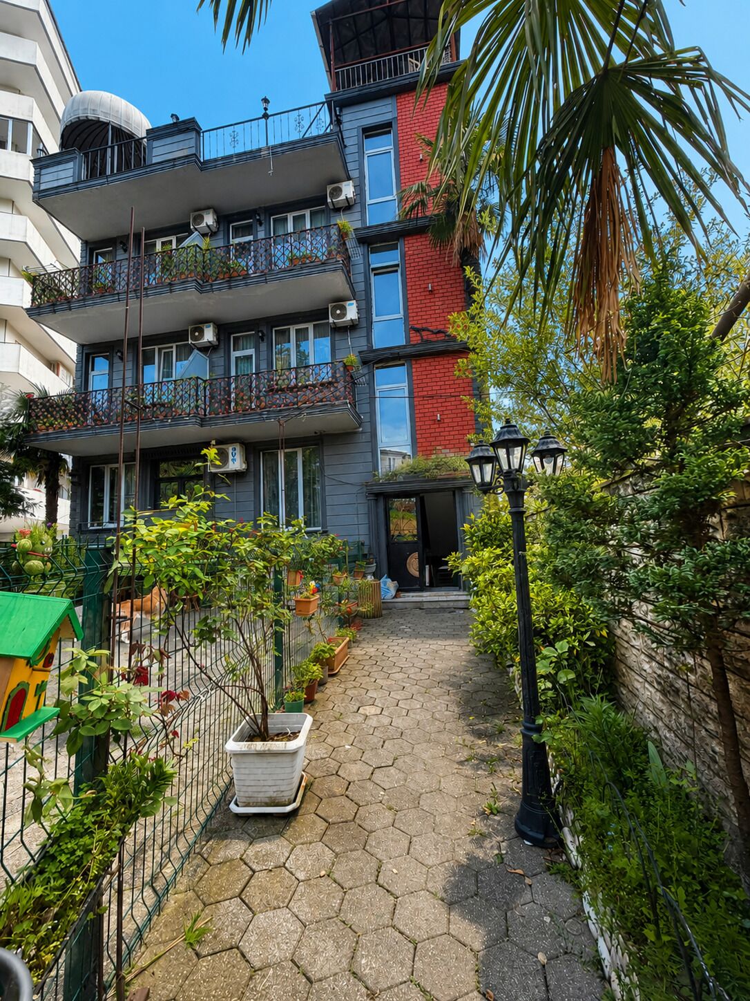 Un immeuble résidentiel à plusieurs étages, doté de balcons, d’un chemin pavé et entouré de verdure.