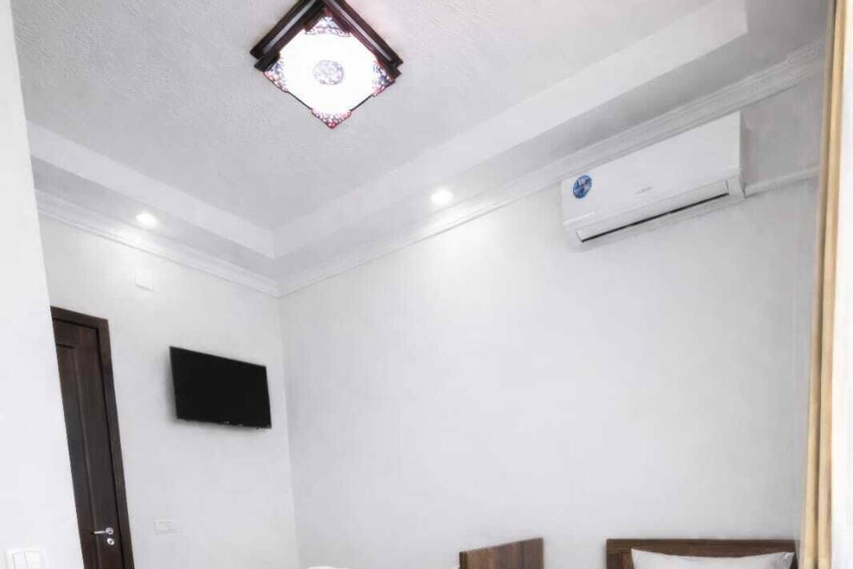 A hotel room with two beds, a TV, an air conditioning unit, and a small kitchenette.