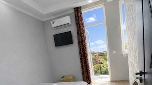 Un dormitorio moderno con cama, mesita de noche, televisor montado en la pared, aire acondicionado y ventana con cortinas.