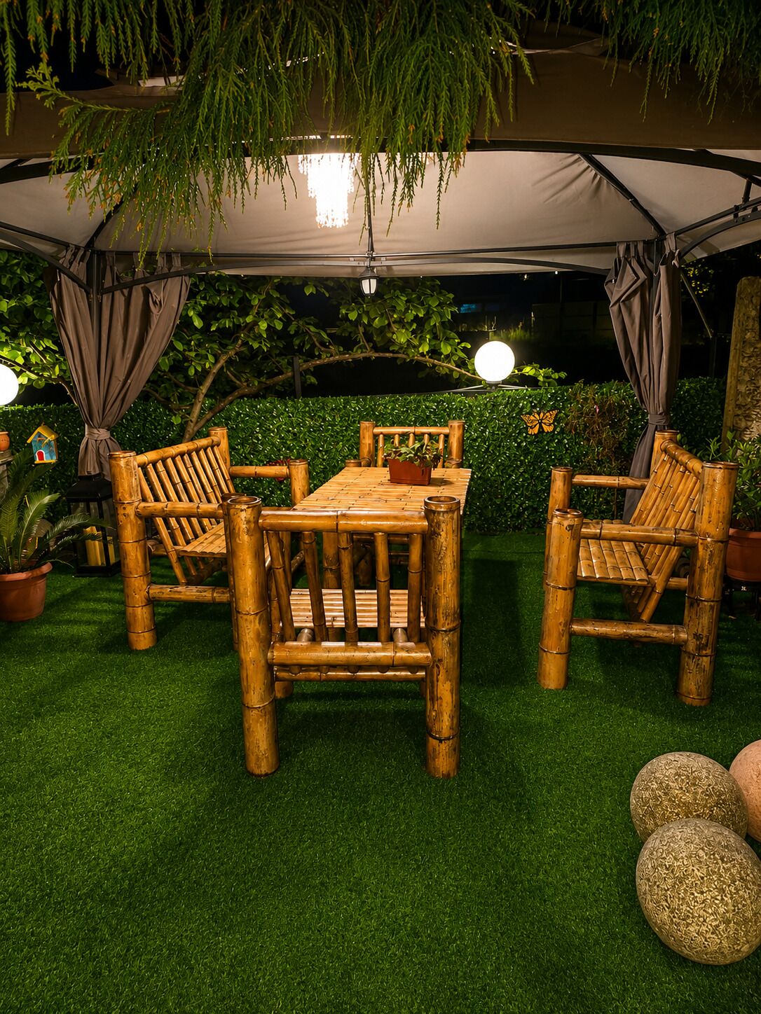 A covered outdoor seating area with a table and chairs, surrounded by greenery and potted plants.