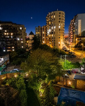 Eine nächtliche Skyline mit Hochhäusern, einem sichtbaren Mond und einer baumbestandenen Fläche.