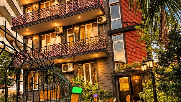 Un edificio de varios pisos con balcones, entrada protegida por una reja y macetas con plantas.