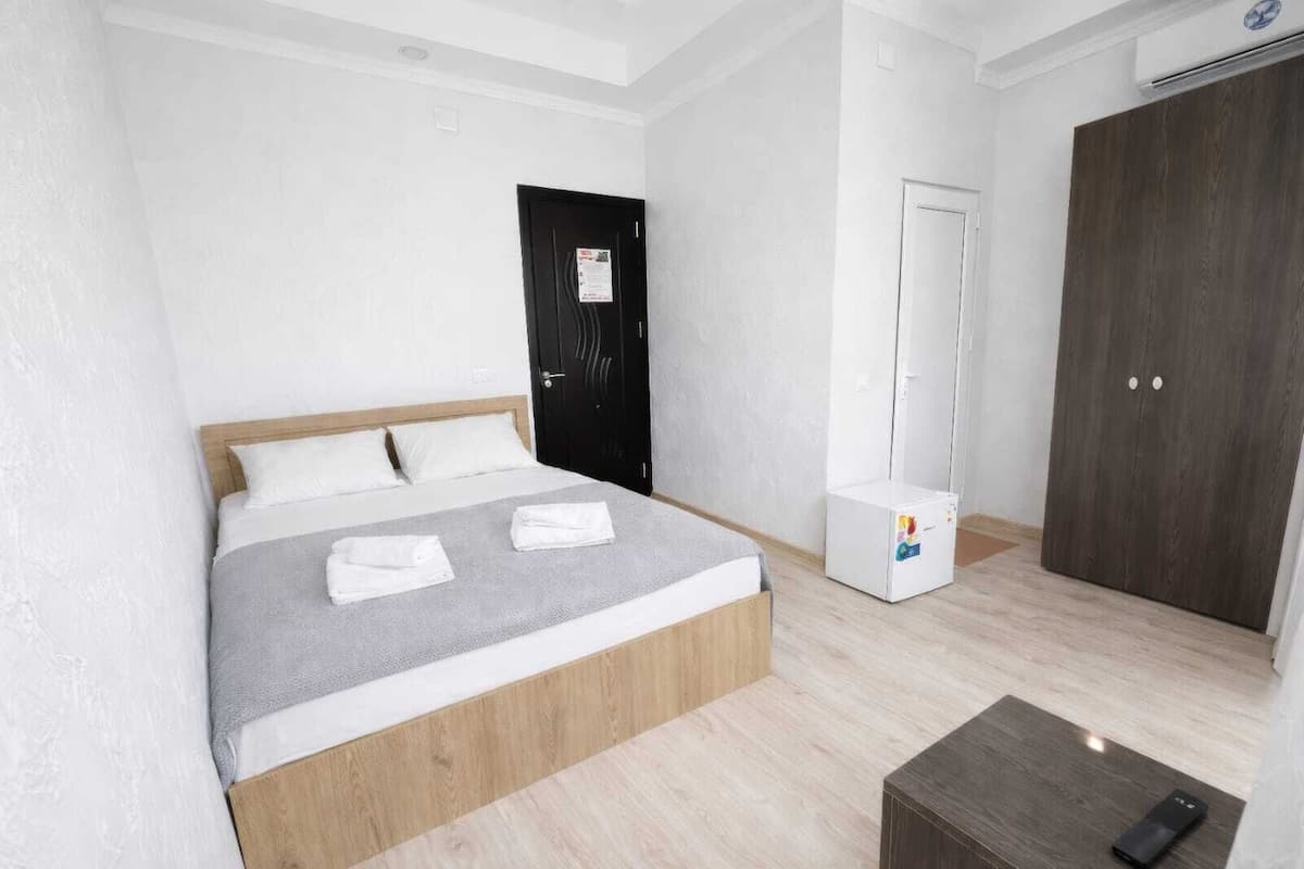 A bedroom with a bed, a wardrobe, a small table, and an air conditioning unit.