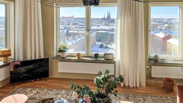 Un salon moderne doté de grandes fenêtres, d’un radiateur, d’un téléviseur à écran plat et de divers objets décoratifs.