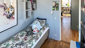 Une petite pièce agréable et chaleureuse, avec un lit simple, une étagère ornée d’objets décoratifs et un tableau au mur.