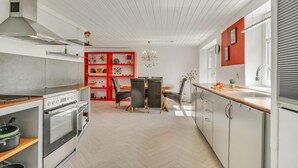 A modern kitchen with white cabinetry, a central island, and a dining area with red shelving. - Stunning home in Grenaa with WiFi (Grenaa)