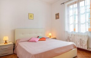 Ein Schlafzimmer mit einem Bett, zwei Nachttischen, einem Fenster mit Vorhängen und zwei an der Wand befestigten Bildern.