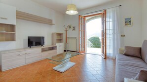 Una sala de estar moderna con una mesa de centro de vidrio, un televisor de pantalla plana, un sofá y un amplio ventanal con vistas a zonas verdes.
