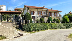 Una casa de dos pisos con fachada de piedra, tejado de tejas y un jardín bien cuidado con setos y una estatua.