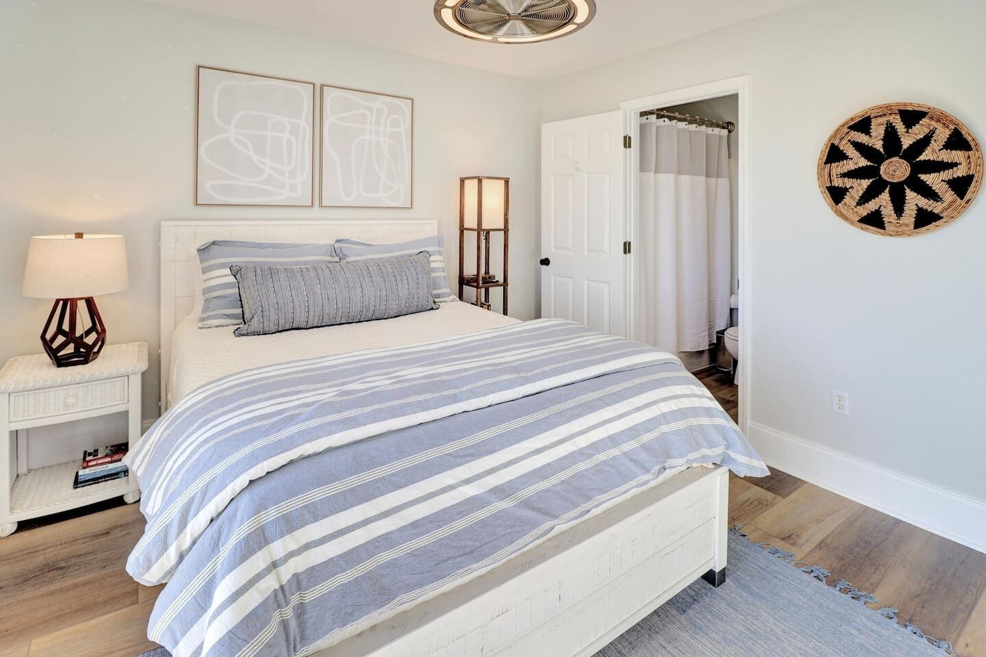Un dormitorio con una cama, mesitas de noche, una lámpara, una puerta y un adorno en la pared.
