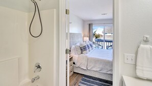 A bathroom with a shower, a bed with pillows, a view of the outside, and a towel on the wall.