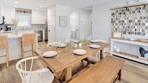 A modern kitchen with white cabinetry, a dining area with a wooden table set for six, and a wall display of ceramic plates.
