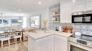 A modern kitchen with white cabinetry, a central island, and a view of the ocean through large windows.