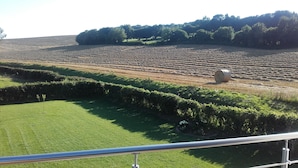 Paisaje rural con un campo de cultivo, un fardo de heno y un seto.