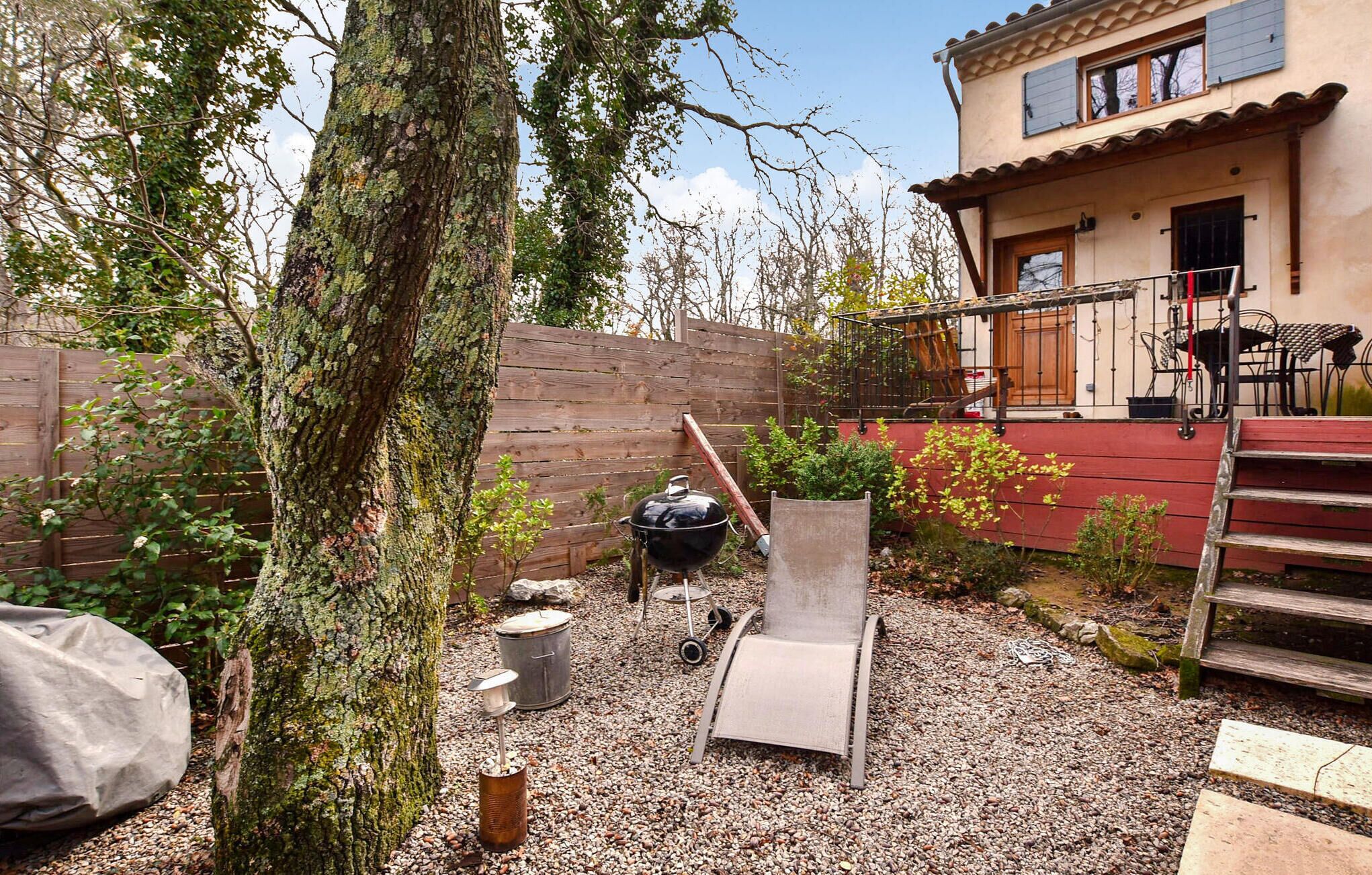 A backyard with a barbecue grill, a wooden deck, a metal chair, and a tree.