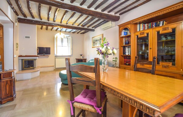 Un coin repas avec une table et des chaises en bois, une bibliothèque remplie de livres et d’objets décoratifs, et une cheminée en arrière-plan.