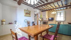 Ein Esszimmer mit Holztisch und Stühlen, einer Vase mit Blumen und einem Fernseher im Hintergrund.