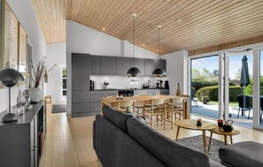 A modern kitchen with a central island, a dining area with a sofa, and a view of the outdoors through large sliding doors. - Beautiful home in ølsted with sauna (Ølsted)
