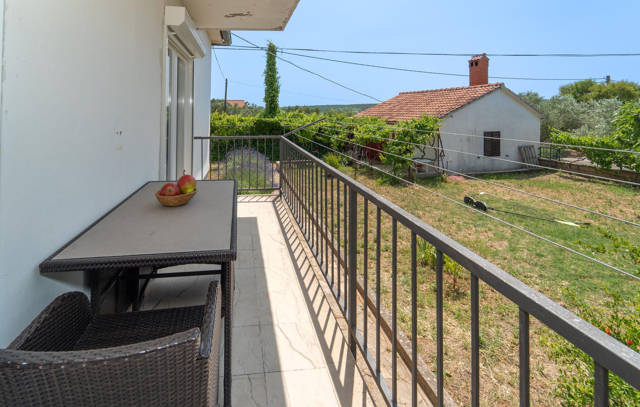 Un balcon avec une table, une chaise en osier et un panier de fruits.
