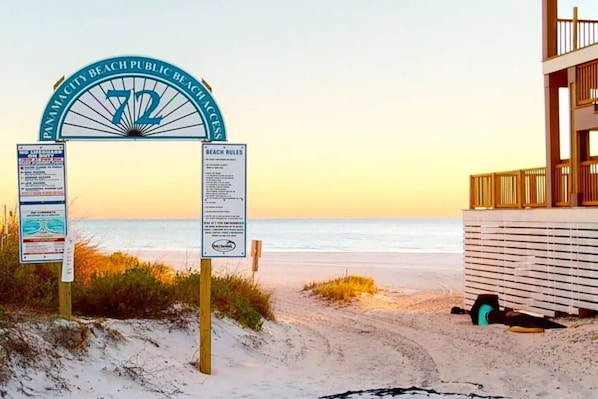 A beach entrance sign with beach rules and a lifeguard warning.