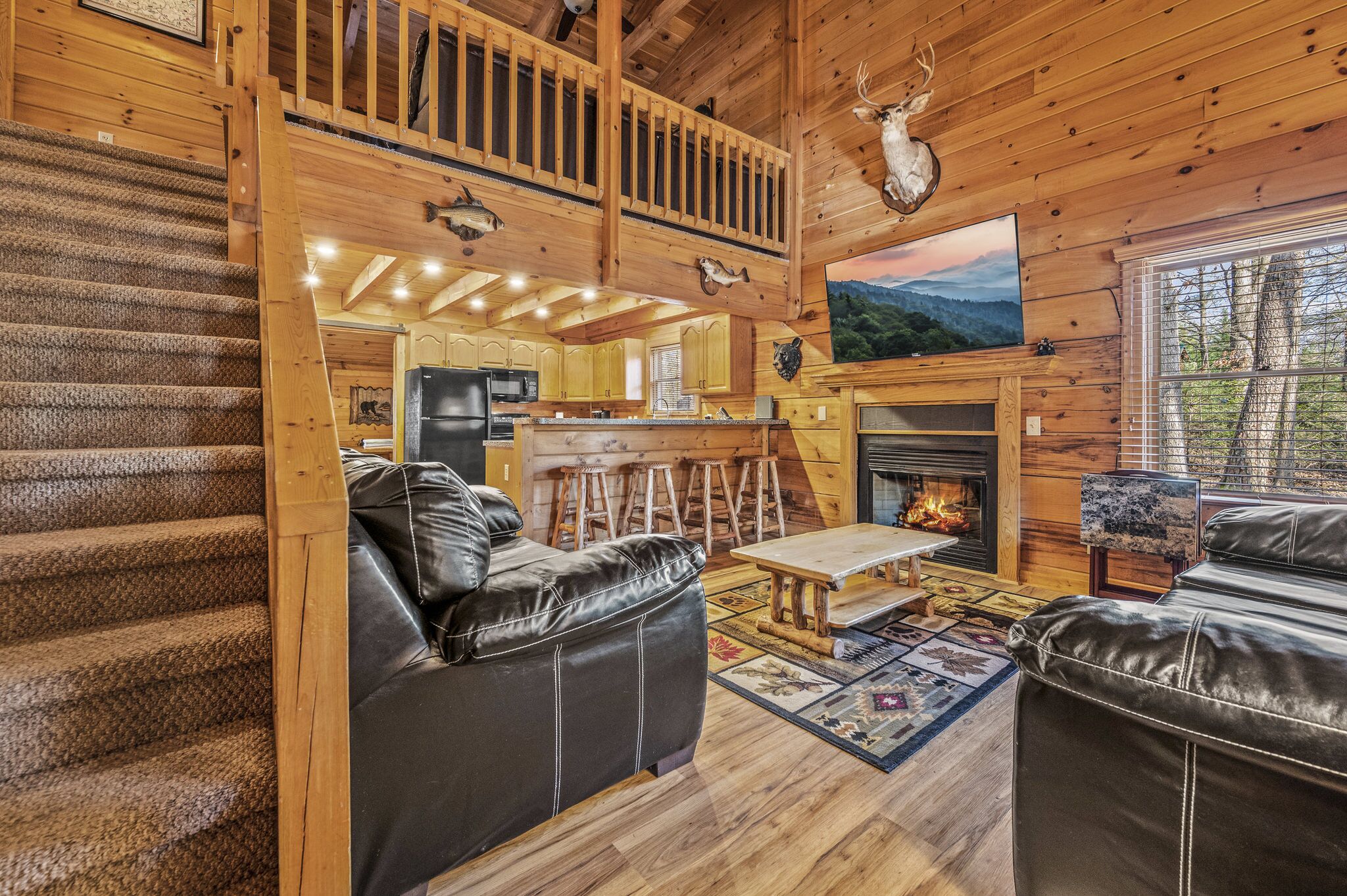 Ein Blockhaus-Interieur mit Kamin, einer Holztreppe, Ledersofas und einer Küchenzeile.