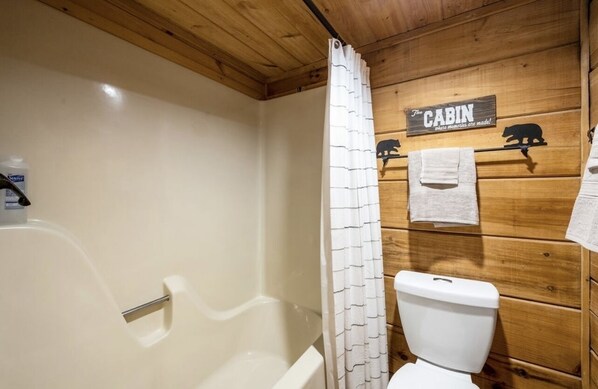 Een houten badkamer in een chalet, met douchegordijn, toilet en een bordje met de tekst 'The Cabin'.