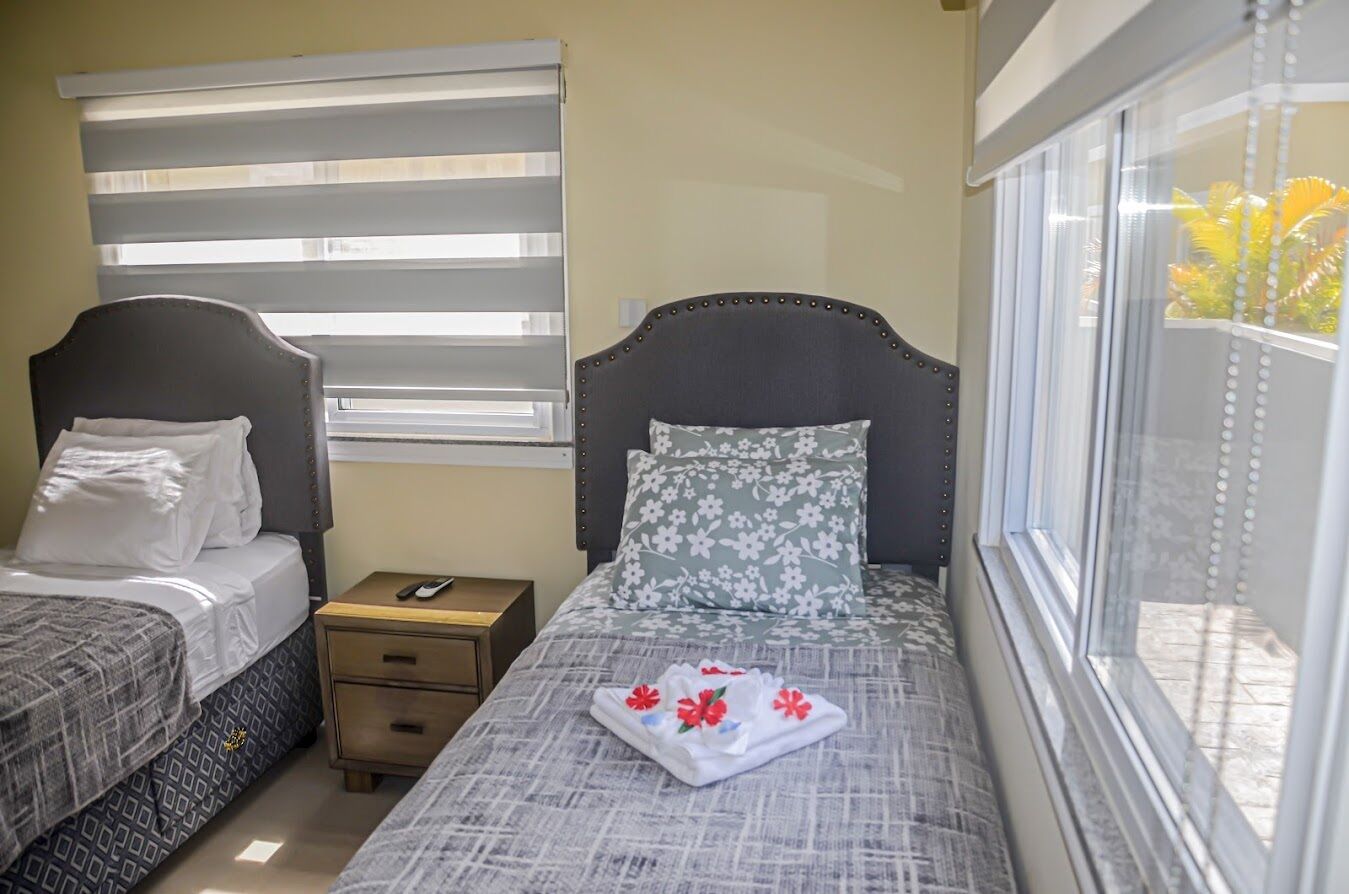 Quarto com duas camas, uma mesa de cabeceira e uma janela com persianas.