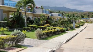 Un hotel moderno con un jardín cuidado, cielo despejado y montañas al fondo.