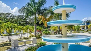 Una fuente de varios niveles con colores azul y blanco, rodeada de palmeras y un paseo empedrado.