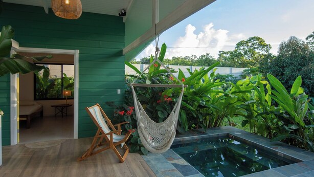 Un espace piscine agrémenté d’un hamac, d’une chaise et d’une végétation luxuriante.