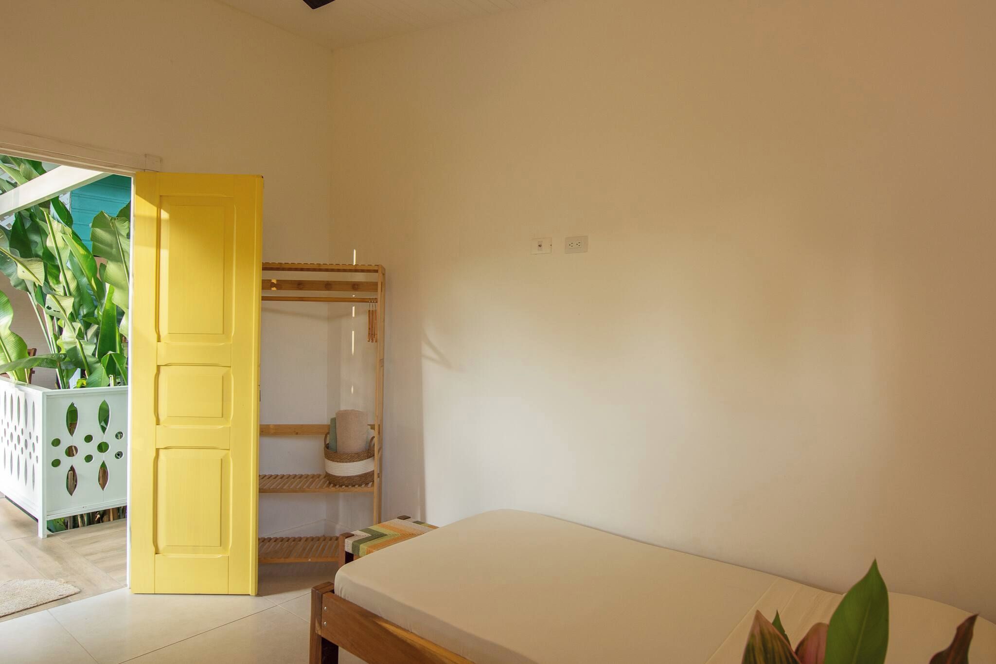 A bedroom with a bed, a yellow door, a mirror, and a plant.