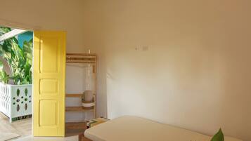 A bedroom with a bed, a yellow door, a mirror, and a plant.