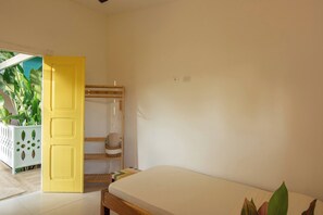 Une chambre à coucher avec un lit, une porte jaune, un miroir et une plante.