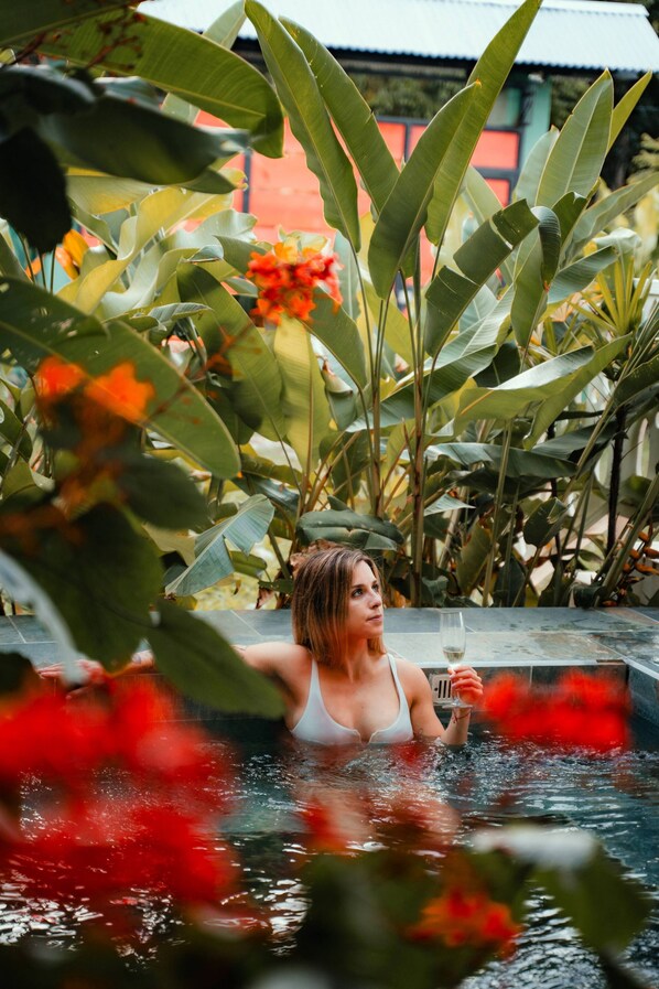 A person in a hot tub surrounded by lush greenery and vibrant flowers.