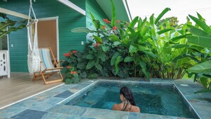 Une personne se détend dans une piscine, avec un hamac et une chaise à proximité, le tout entouré d’une végétation luxuriante.
